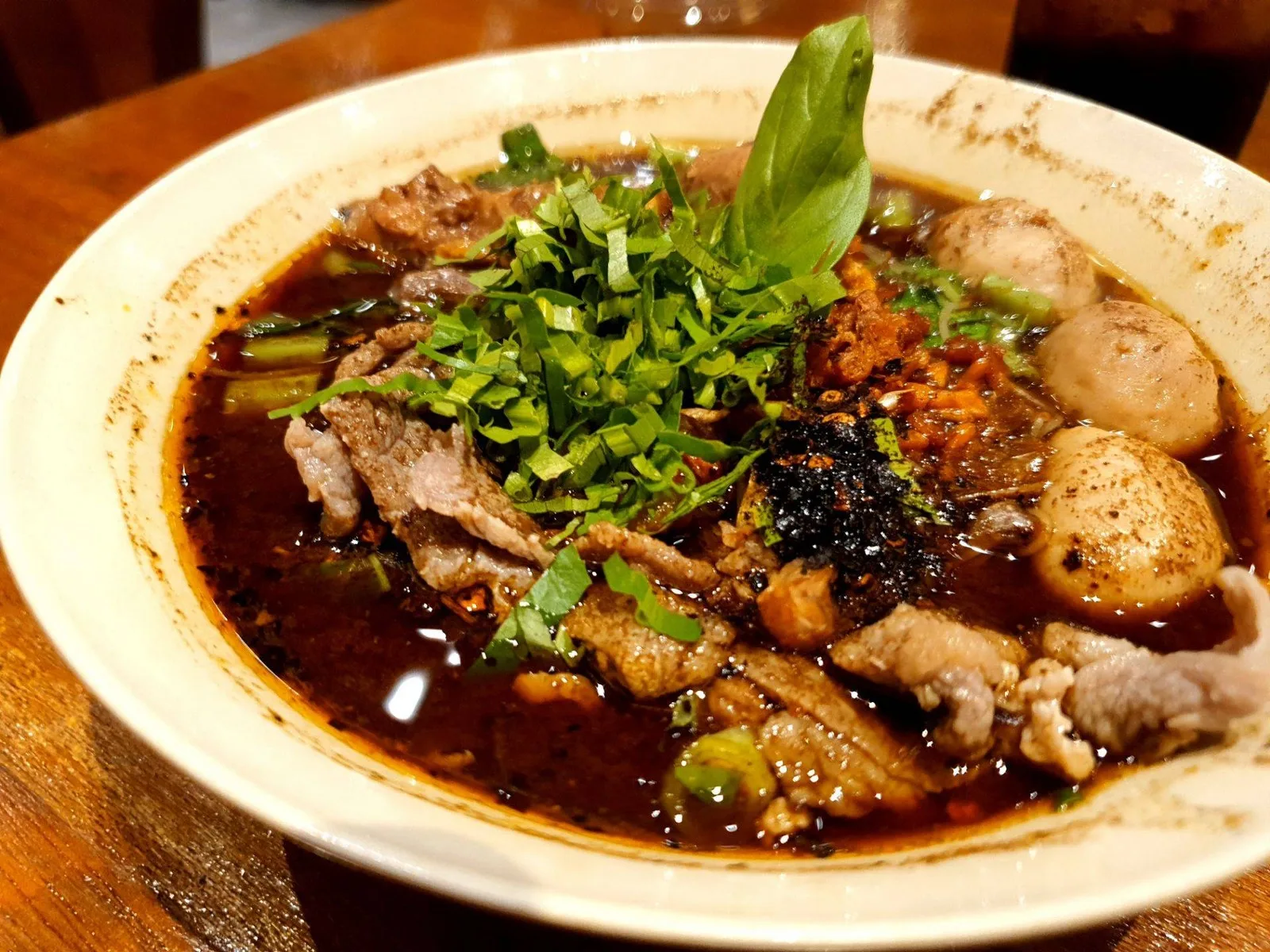 ก๋วยเตี๋ยวเนื้อน้ำตกในชามกระเบื้อง น้ำซุปสีเข้ม โรยโหระพาและผักชีฝรั่ง