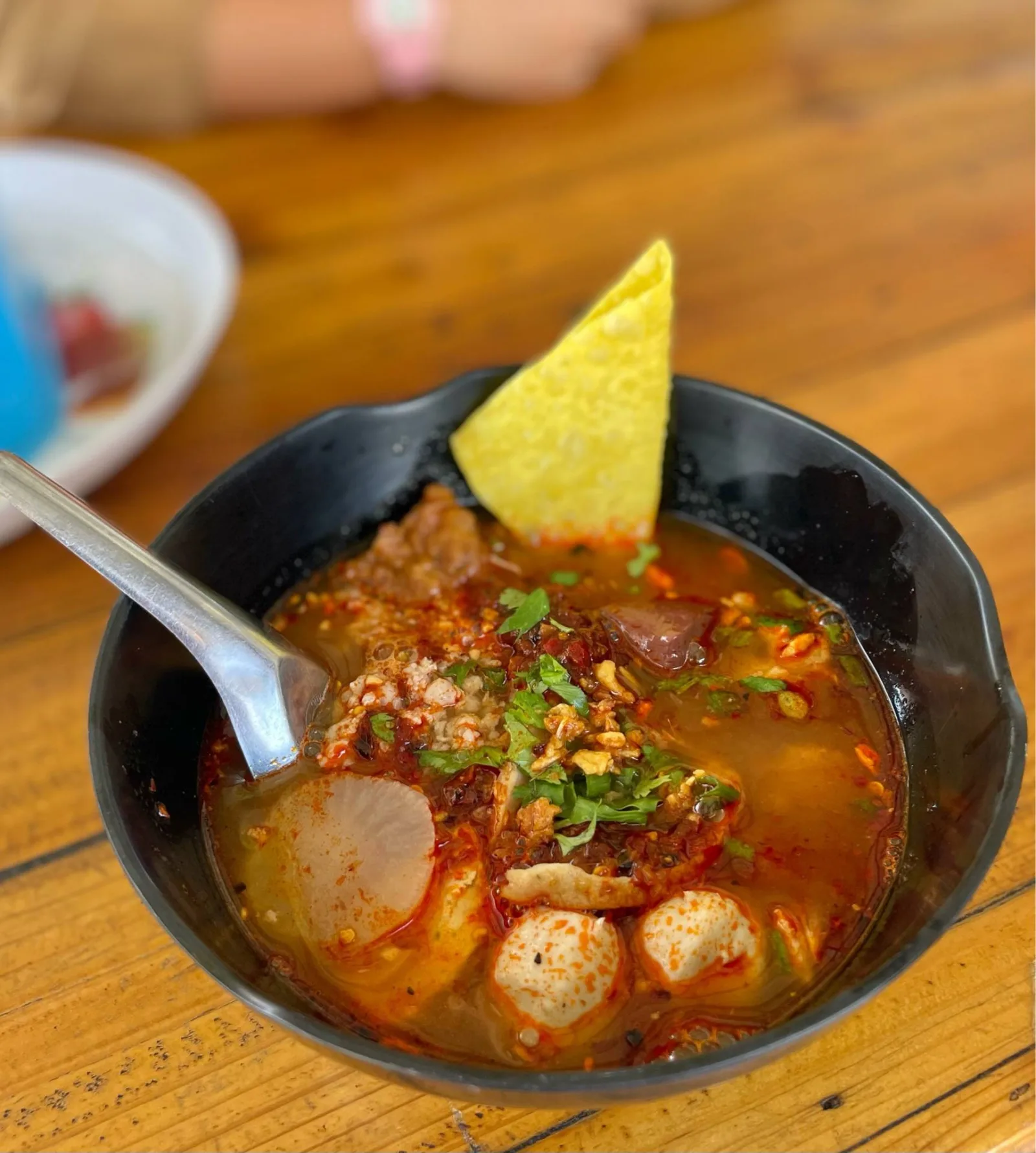ก๋วยเตี๋ยวเนื้อต้มยำในชามดำ น้ำซุปสีส้ม มีเกี๊ยวกรอบวางพาด